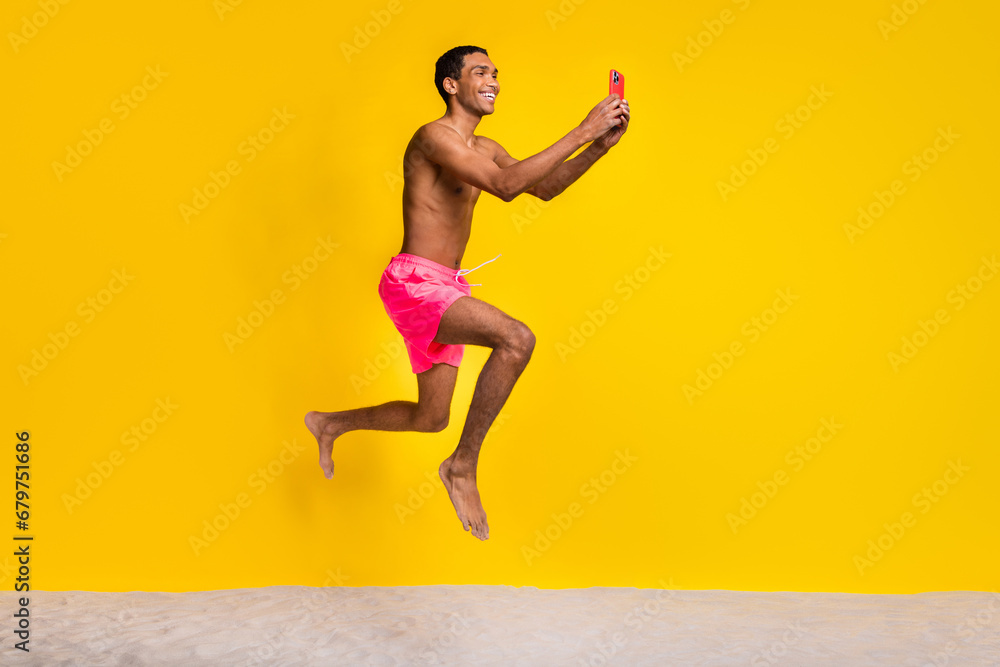 Full length photo of pretty positive shirtless man jumping high texting instagram twitter telegram facebook isolated yellow color background