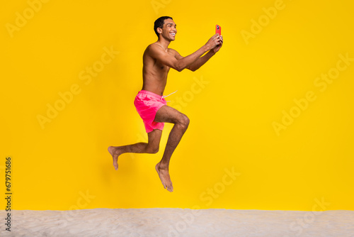 Full length photo of pretty positive shirtless man jumping high texting instagram twitter telegram facebook isolated yellow color background