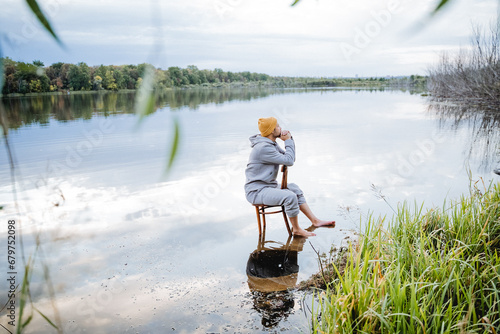 A man is sitting on a chair in the water, a guy in a yellow hat is posing for an art photographer. Soak your feet in the cold water of the lake.