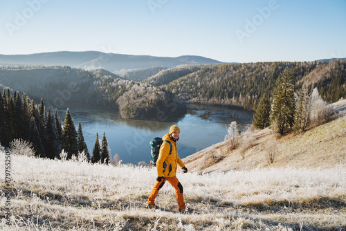 Man with backpack walking on the mountains against the background of an icy lake, mountain trekking in winter, cold season, outdoor vacation, autumn hike.