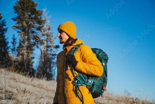 A guy with a backpack in a yellow jacket stands against the background of a blue sky. Mountaineer before climbing, nature vacation, trekking in the mountains.