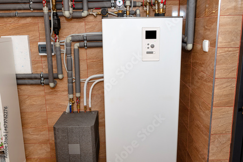 A modern air heat pump installed in the home's boiler room, visible plastic pipes and valves. photo