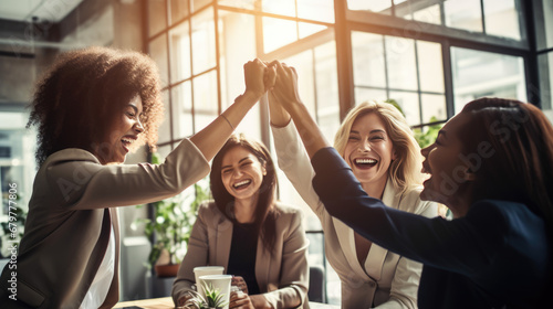 Moment of celebration, with a group of women in a business setting giving each other a high five, all smiling and exuding happiness and a sense of achievement. photo