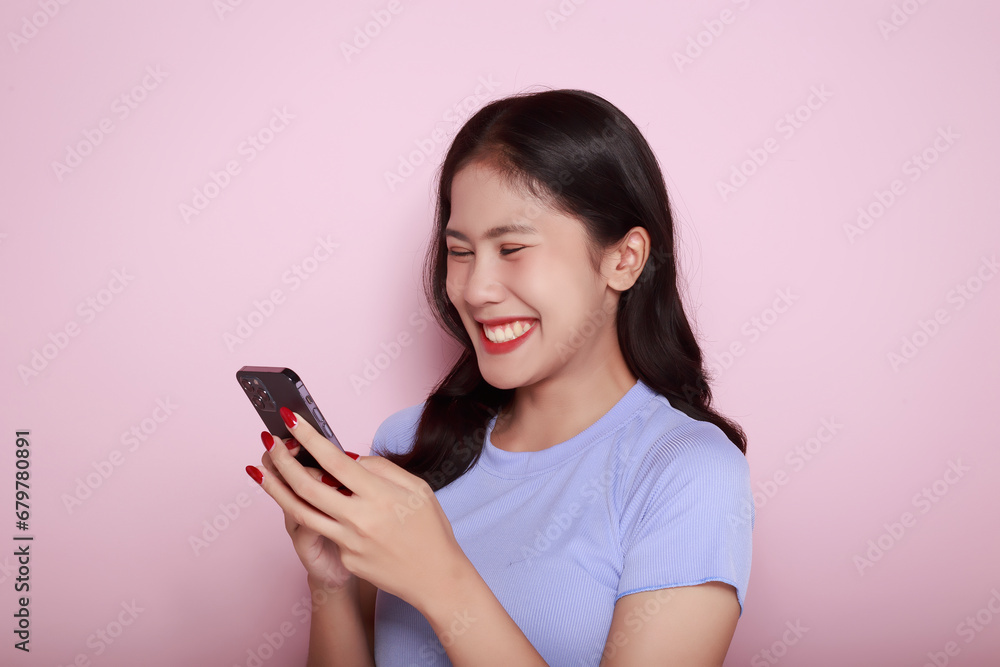 Posing alone on a light pink background. Asian woman is excited about something on the phone The young woman felt extremely happy. half body photo of nice positive lady. Posing alone on a light pink background. Asian woman is excited about something on the phone The young woman felt extremely happy. half body photo of nice positive lady.