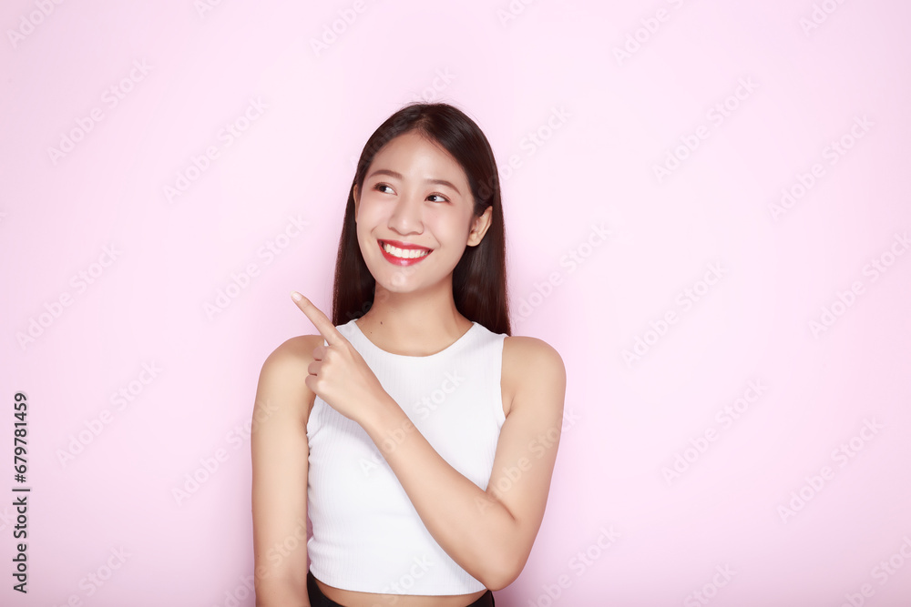 Standing and pointing happily, Portrait of a beautiful young woman in a light pink background, happy and smile, posting in stand position. Standing and pointing happily, Portrait of a beautiful young woman in a light pink background, happy and smile, posting in stand position.