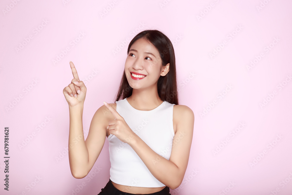 Standing and pointing happily, Portrait of a beautiful young woman in a light pink background, happy and smile, posting in stand position. Standing and pointing happily, Portrait of a beautiful young woman in a light pink background, happy and smile, posting in stand position.