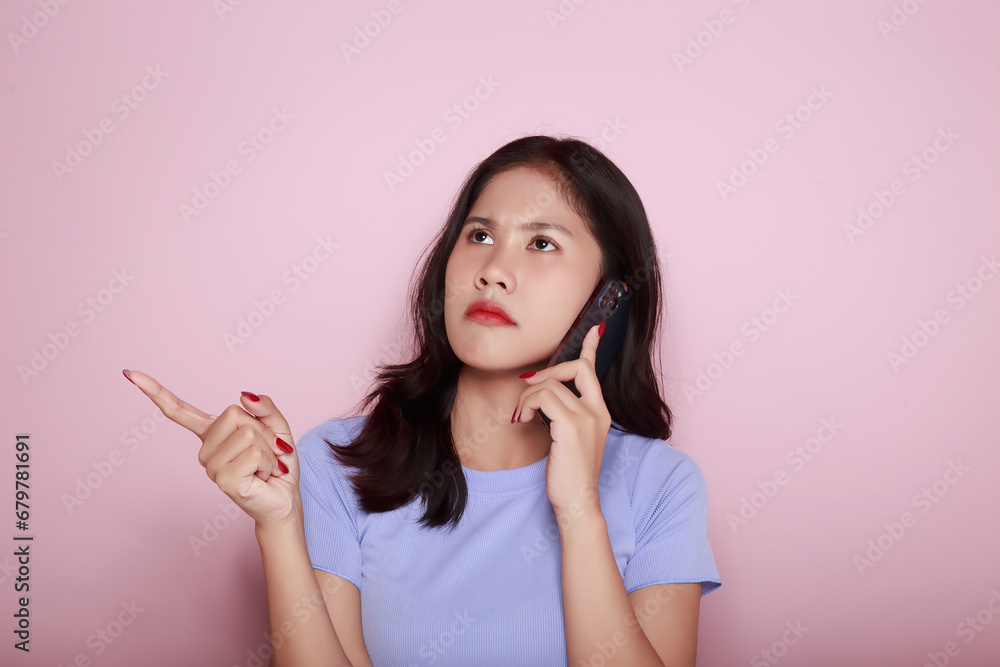 Young woman using the mobile with a serious expression, Portrait of a beautiful young woman in a light pink background, Asian woman posing using a mobile phone. Young woman using the mobile with a serious expression, Portrait of a beautiful young woman in a light pink background, Asian woman posing using a mobile phone.