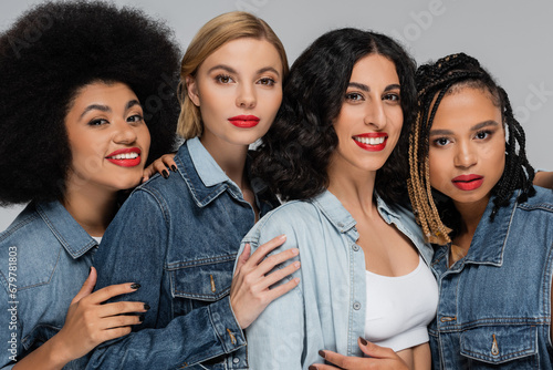 group portrait of multiethnic girlfriends in denim wear looking at camera on grey, diverse beauty