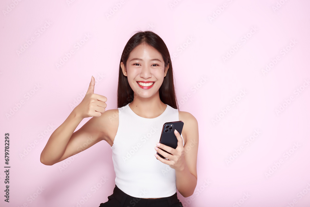 Portrait of a beautiful young woman in a light pink background, happy and smile, posting in stand position, Asian woman looks surprised while holding phone in hand Portrait of a beautiful young woman in a light pink background, happy and smile, posting in stand position, Asian woman looks surprised while holding phone in hand