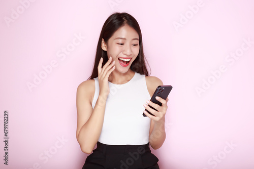 Portrait of a beautiful young woman in a light pink background, happy and smile, posting in stand position, Asian woman looks surprised while holding phone in hand