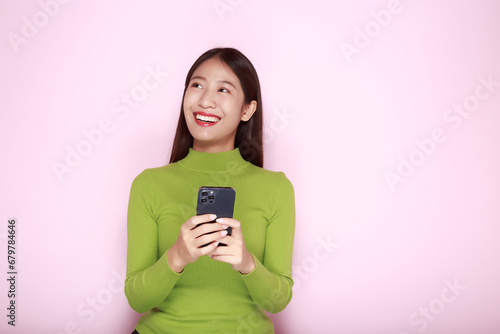 Portrait of a beautiful young woman in a light pink background, happy and smile, posting in stand position, Asian woman looks surprised while holding phone in hand