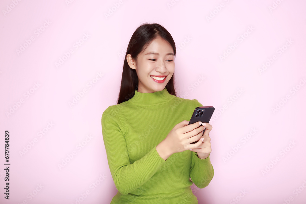 Portrait of a beautiful young woman in a light pink background, happy and smile, posting in stand position, Asian woman looks surprised while holding phone in hand Portrait of a beautiful young woman in a light pink background, happy and smile, posting in stand position, Asian woman looks surprised while holding phone in hand