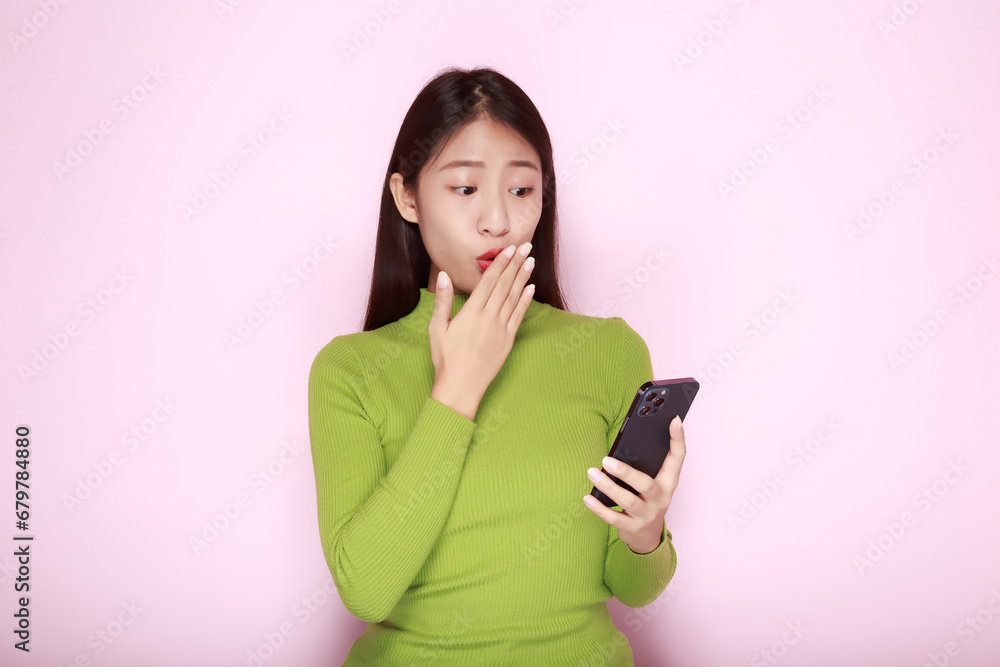 Portrait of a beautiful young woman in a light pink background, happy and smile, posting in stand position, Asian woman looks surprised while holding phone in hand Portrait of a beautiful young woman in a light pink background, happy and smile, posting in stand position, Asian woman looks surprised while holding phone in hand