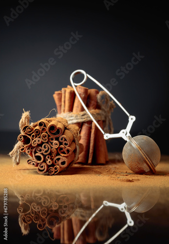 Ground cinnamon, cinnamon sticks, tied with jute rope on a black reflective background.