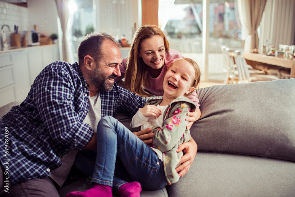 Parents having fun with small child daughter on couch at home