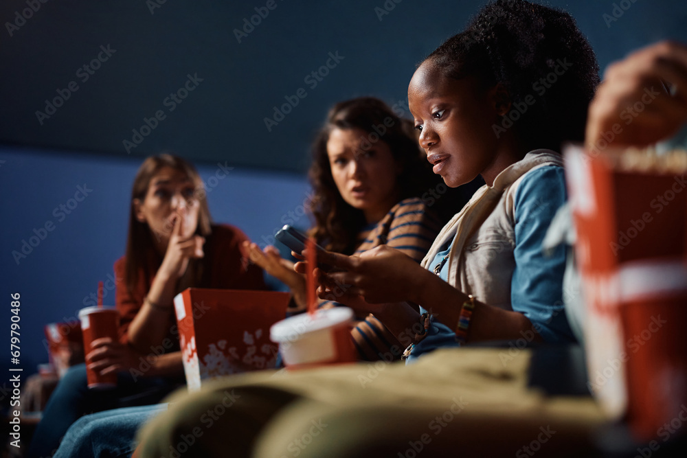 Black woman using cell phone during movie projection in cinema. Black woman using cell phone during movie projection in cinema.