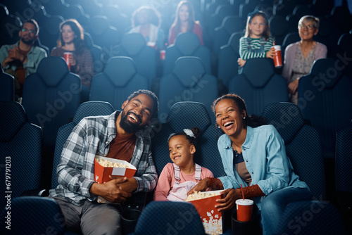 Happy black parents and their daughter watching movie in cinema.