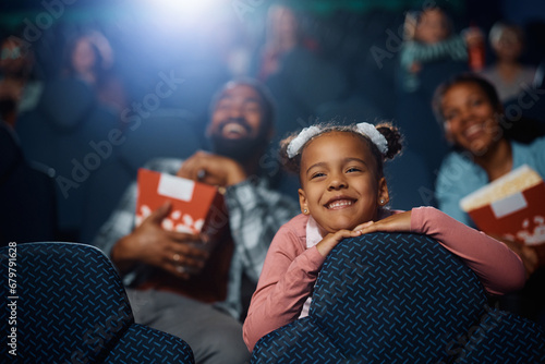 Smiling African American girl watching movie with her parents in cinema.