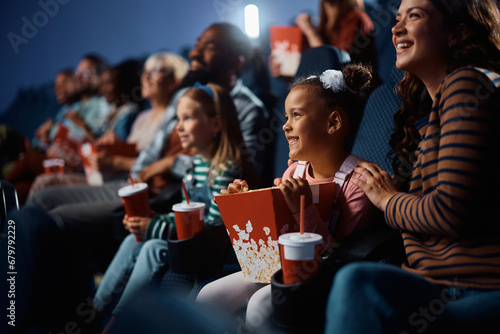 Happy black little girl watching movie with her family in theater.