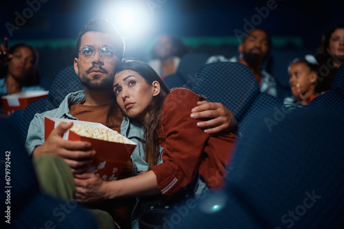 Young couple embracing while watching suspenseful movie in theater.
