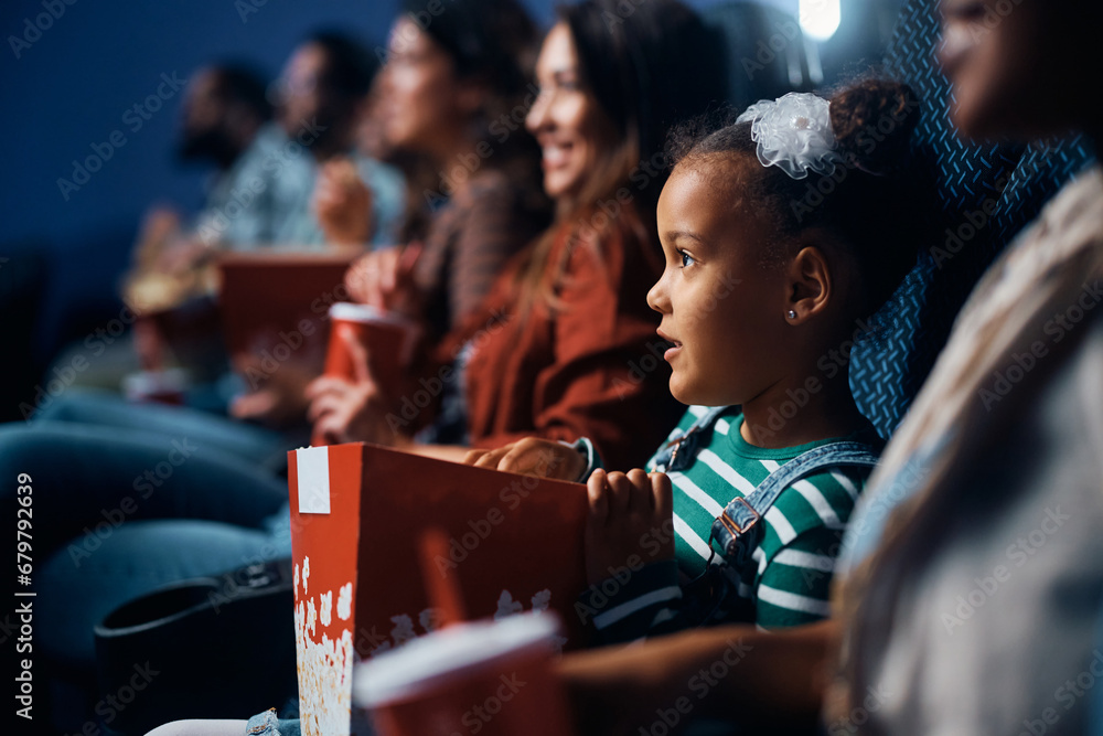 black little girl eats popcorn during movie projection in cinema. - obrazy, fototapety, plakaty 