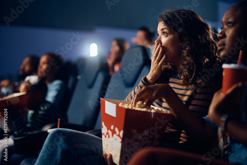 Shocked woman watching suspenseful movie in theater.
