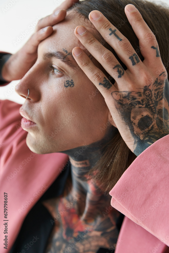Obraz premium portrait of young fashionable man with tattoos on face and piercing with hands on face looking away