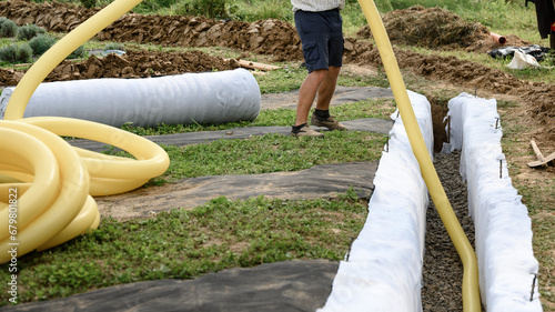 A worker carries a yellow perforated drainage pipe. Groundwater drainage works in the field photo