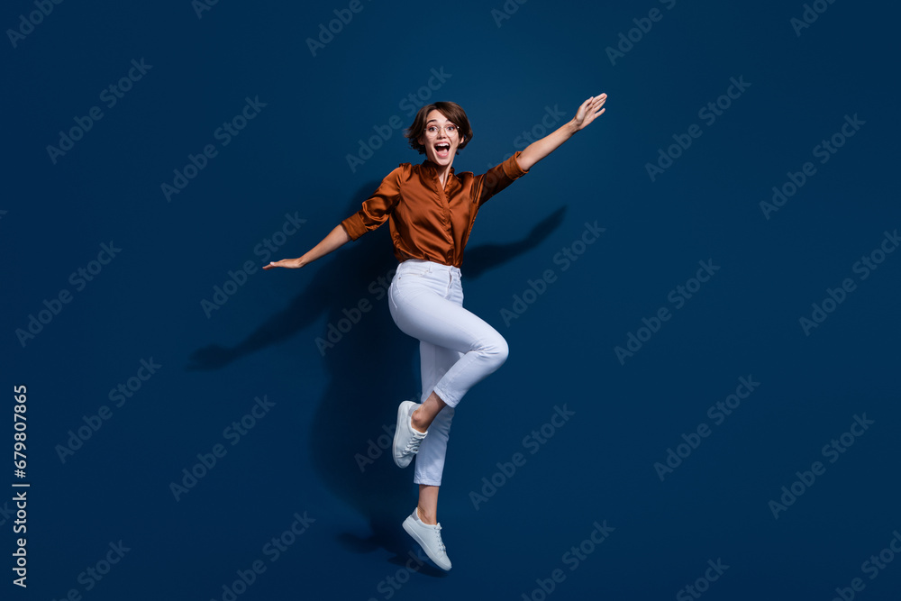 Full length photo of carefree sweet lady wear brown shirt glasses jumping high having fun isolated blue color background