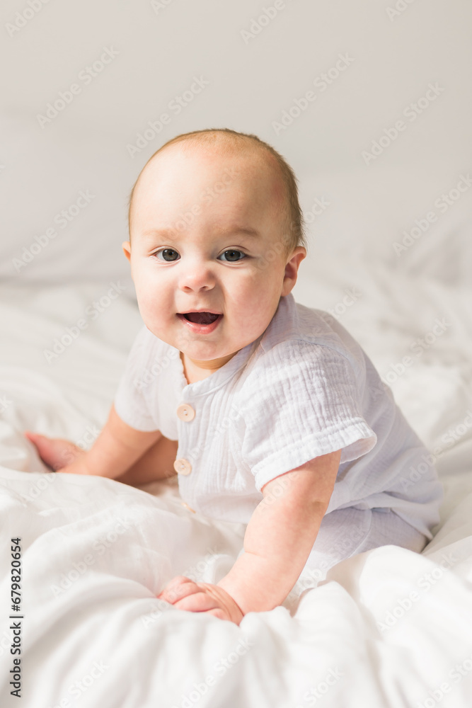 Adorable baby boy in white sunny bedroom. Newborn child relaxing in bed. Nursery for young children. Textile and bedding for kids. Family morning at home. Adorable baby boy in white sunny bedroom. Newborn child relaxing in bed. Nursery for young children. Textile and bedding for kids. Family morning at home.