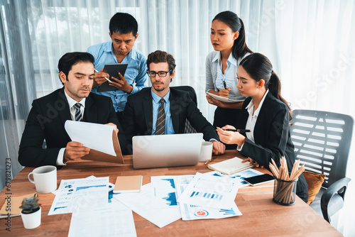 Diverse group of business analyst team analyzing financial data report paper on office table. Chart and graph dashboard by business intelligence analysis for strategic marketing planning Habiliment