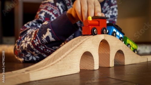 Closeup of boy in pajamas lying on floor and playing with toy wooden train and railroad. photo