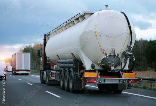 Petrol cargo truck driving on highway hauling oil products. Fuel delivery transportation. Aviation fuel transportation. Compressed gas carrier truck rear view on a highway. Dairy products carrier