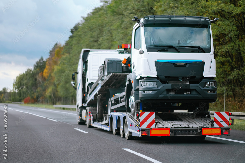 A side view of the towing truck with a brand-new commercial vehicle for cargo shipping. Emergency roadside assistance. Vehicle Mechanical Problem on the Road. Warranty case. Bill of Loading Manifest.