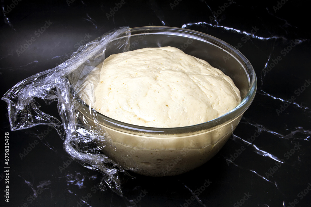 yeast dough in a transparent plate on a black marble background