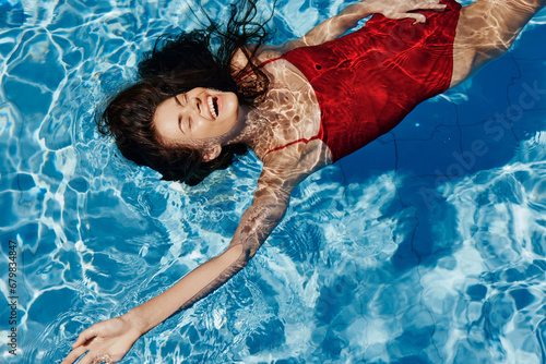 Young woman in the pool in a red swimsuit with a beautiful smile lying on the water and swimming in the sun swimming in the pool, the concept of relaxing on vacation. photo