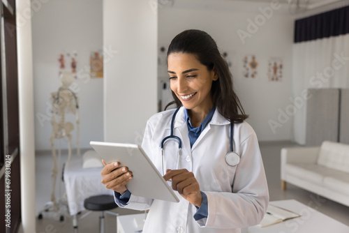 Positive young Latin medical therapist woman working with digital tablet, using gadget for communication with patients, online medical consultation, smiling. Female doctor giving help on Internet