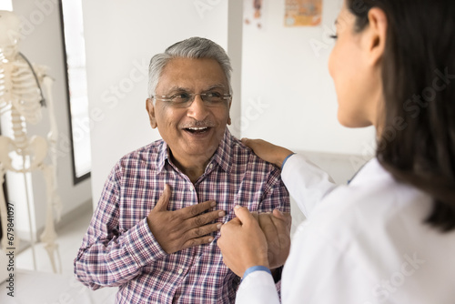 Young doctor woman calming senior Indian patient, holding mans hand, touching shoulder with comfort, support, compassion, telling good news about health, heart work