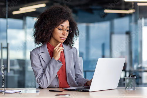 Serious focused and concentrated woman at workplace, thinking businesswoman looking at laptop screen, working inside office at workplace, solving financial technical tasks