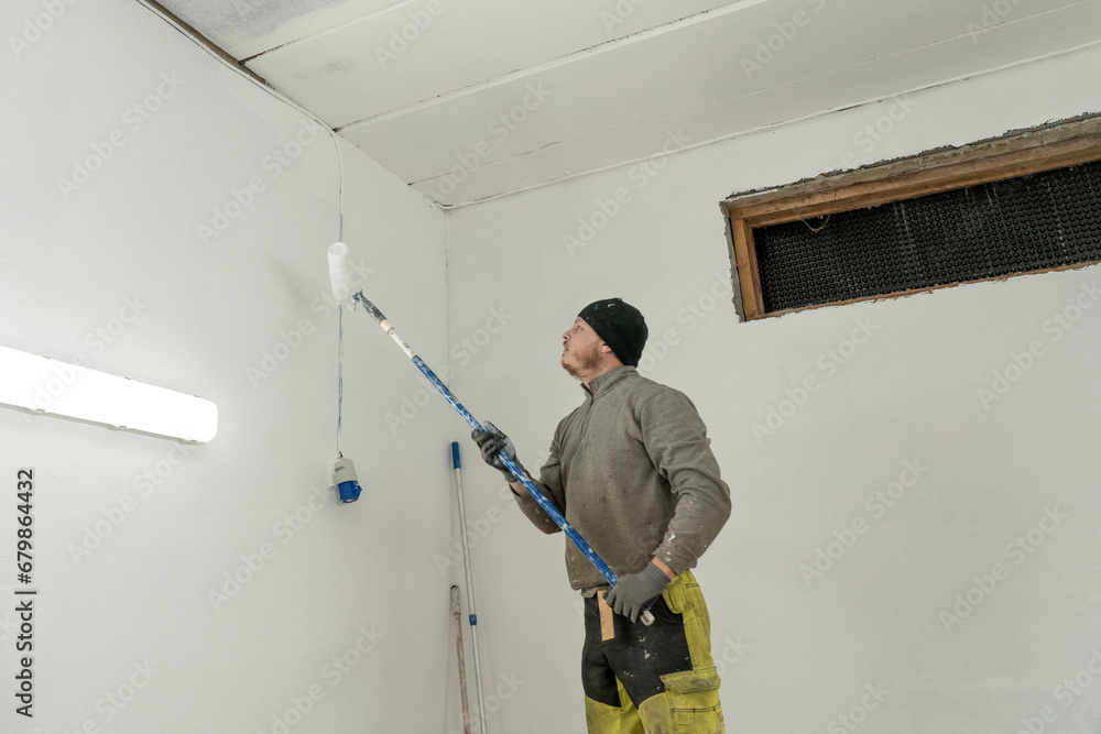 Dedicated Craftsman in Work Clothes Adds Final Touches to White Garage Painting. Dedicated Craftsman in Work Clothes Adds Final Touches to White Garage Painting.