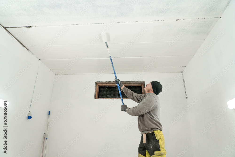 Diligent Worker in Grey Jumper and Yellow Trousers Adds Final Strokes to White Garage Paint Job. Diligent Worker in Grey Jumper and Yellow Trousers Adds Final Strokes to White Garage Paint Job.