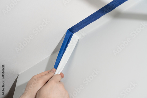 Flawless Finish: Man's Hand Expertly Removes Paint Tape, Revealing Perfectly Coated Room Corners. photo