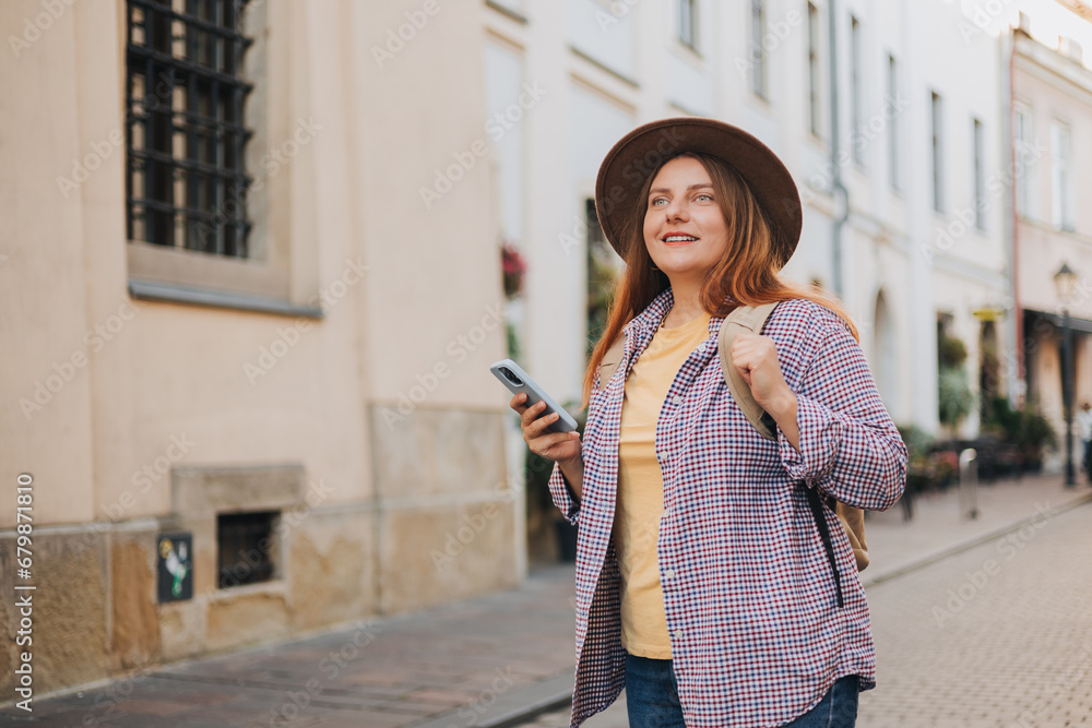 Picture of pretty young woman staying on the street holding phone in hands. 30s tourist walking on old city street checks her smartphone. Use technology concept, Traveling Europe in spring