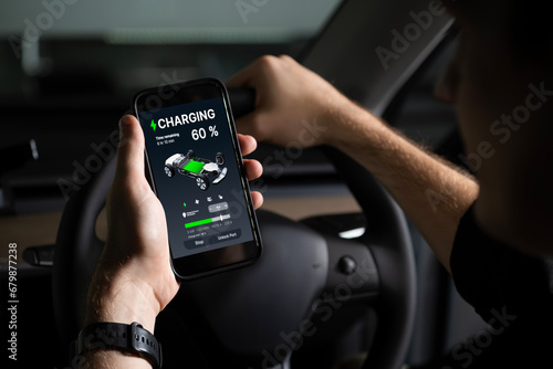 Electric car driver checks battery charging status, range and charging limit on app screen in the car. Smart technology device show EV car recharging data of electric storage in car battery innards. photo