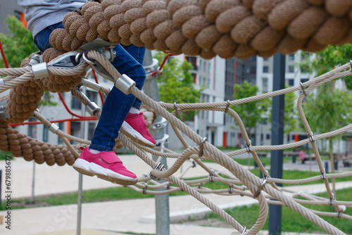 Child sits on a rope on a playground in the courtyard of an apartment building.