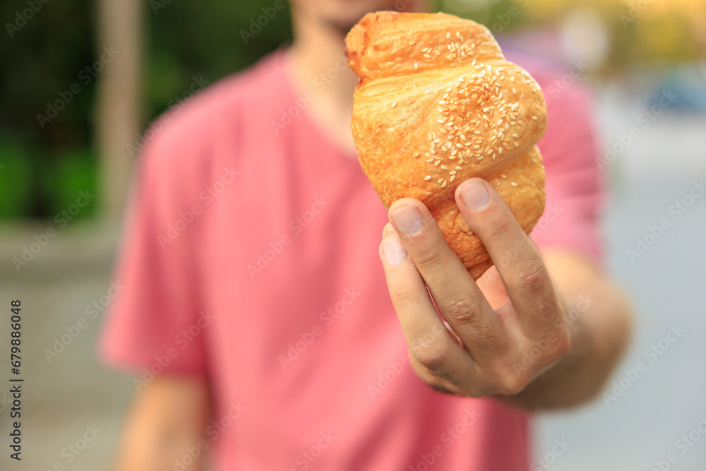 Guy's hand holds a croissant, snack and fast food concept. Selective focus on hands with blurred background