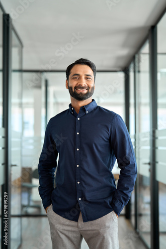 Professional smiling businessman manager executive or male employee or entrepreneur vertical portrait. Happy bearded Indian business man leader looking at camera standing in office hallway.
