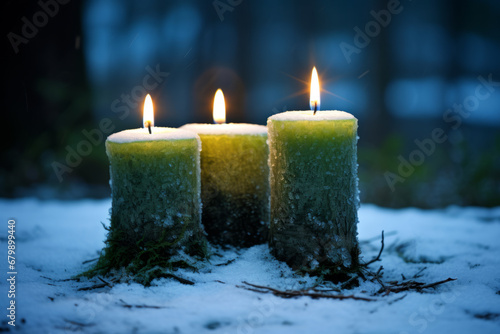 Three green candles are lit in the snow. The candles are tall and slender, with pointed flames that flicker in the breeze