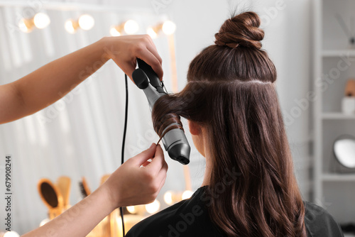 Hairdresser using curling hair iron while working with woman in salon, closeup