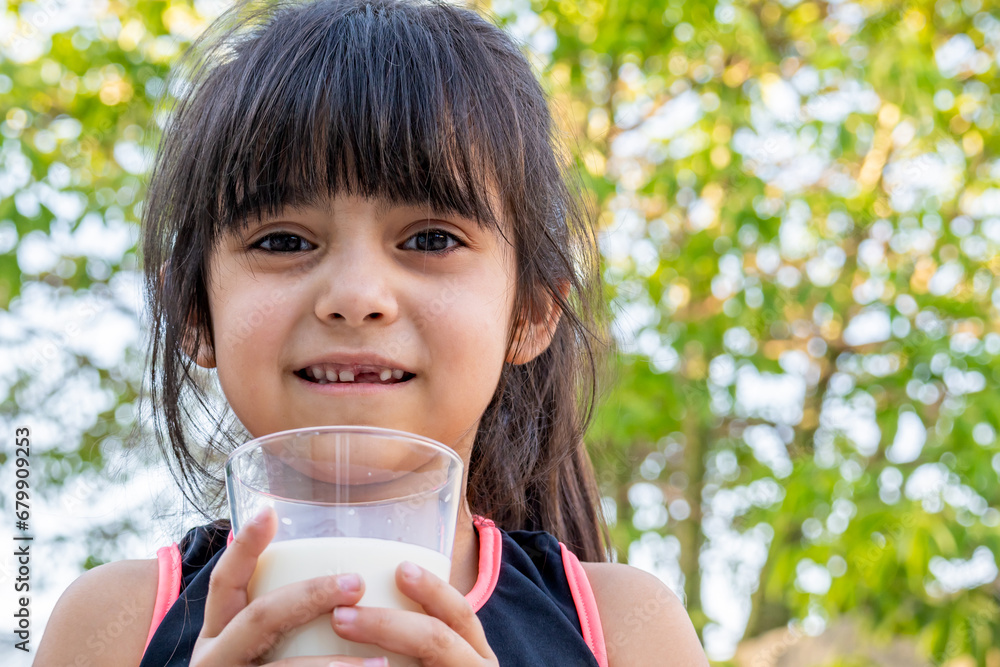 Close-up portrait of her. She drinks a glass of cold milk after playing outside her house. Close-up portrait of her. She drinks a glass of cold milk after playing outside her house.
